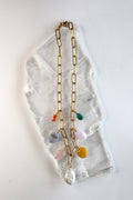 Elavene 18K gold-plated paperclip chain necklace by Auréád Designs laid flat on a white selenite slab, displaying seven mixed gemstone charm drops including orange aventurine, blue lace agate, rose quartz, freshwater pearl, yellow jade, lavender amethyst, and malachite