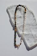 Equina necklace by Auréad Designs, featuring blue tiger eye tube beads and oval freshwater pearls on a white silk-knotted strand with a 14k gold-filled toggle clasp, laid flat on a white selenite slab