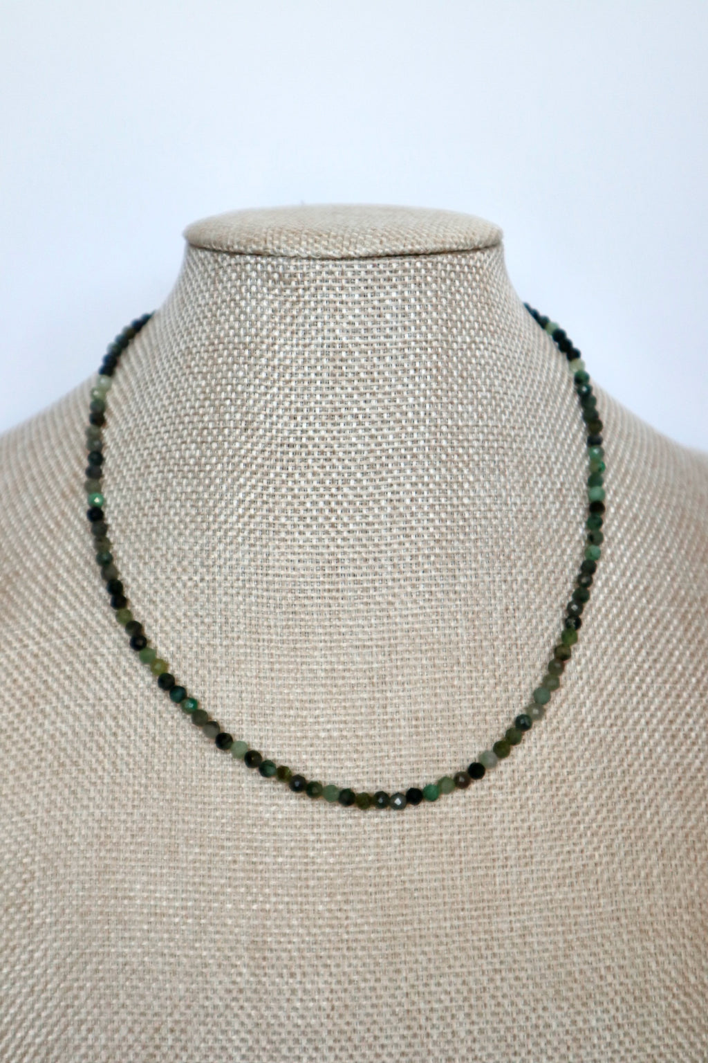 Auréad Designs Esmira necklace displayed front-facing on linen bust form, continuous strand of 3mm faceted emerald beads sitting at collarbone length