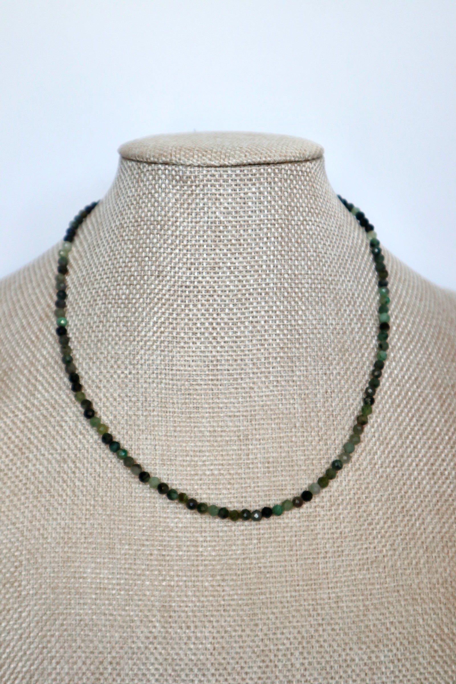 Auréad Designs Esmira necklace displayed front-facing on linen bust form, continuous strand of 3mm faceted emerald beads sitting at collarbone length