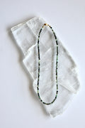 Auréad Designs Esmira necklace laid flat on white selenite slab, showing full strand of 3mm faceted round emerald beads with gold stainless steel lobster clasp