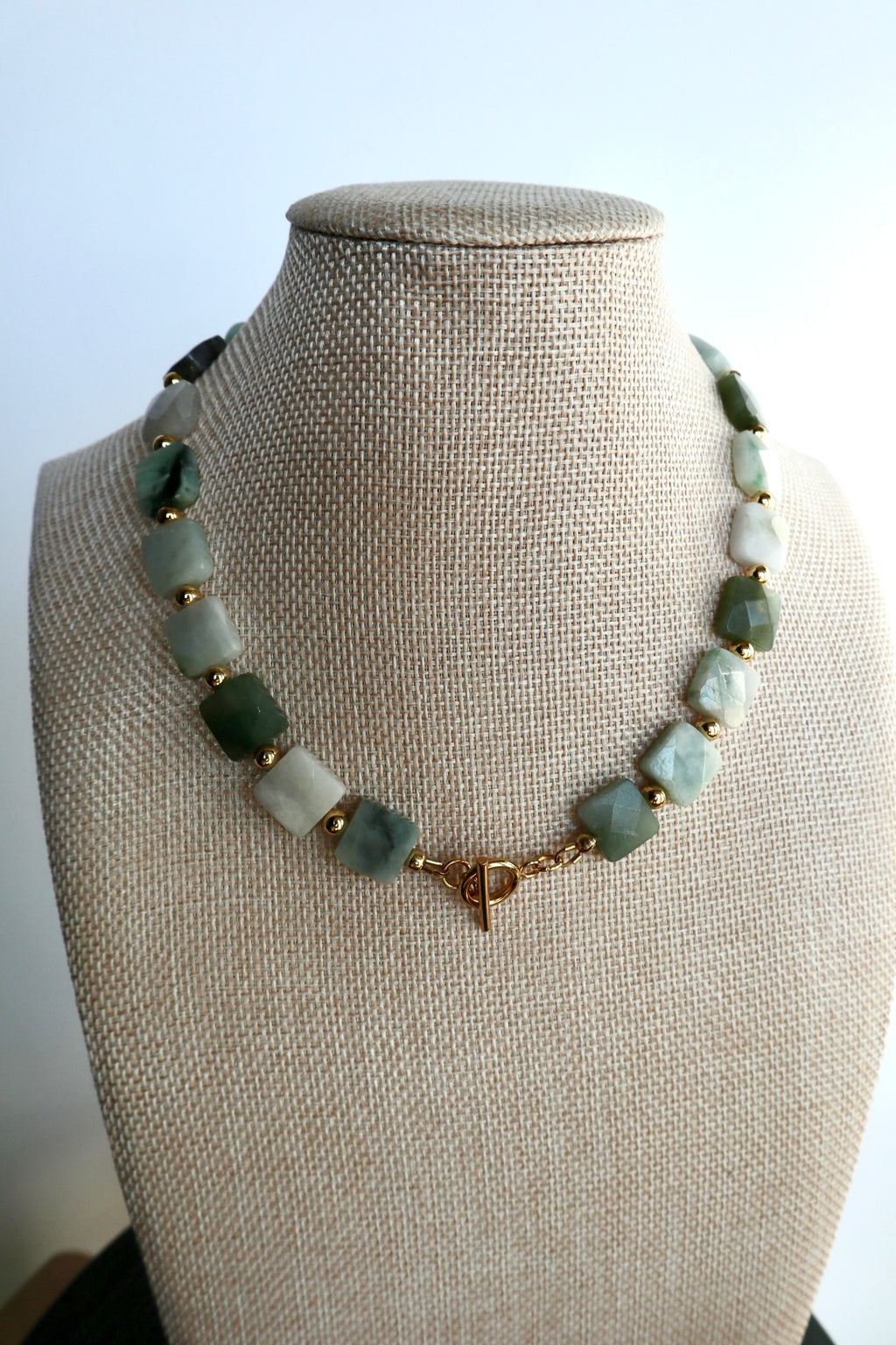 Everra necklace by Auréad Designs displayed on a linen bust form, showing the full sculptural strand of square nephrite jade beads and gold stainless steel spacers with toggle clasp