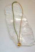 Florae necklace by Auréad Designs, featuring faceted peridot gemstone beads, a 14k gold-filled cable chain, and a gold flower pendant with a lobster clasp, laid flat on a white selenite slab