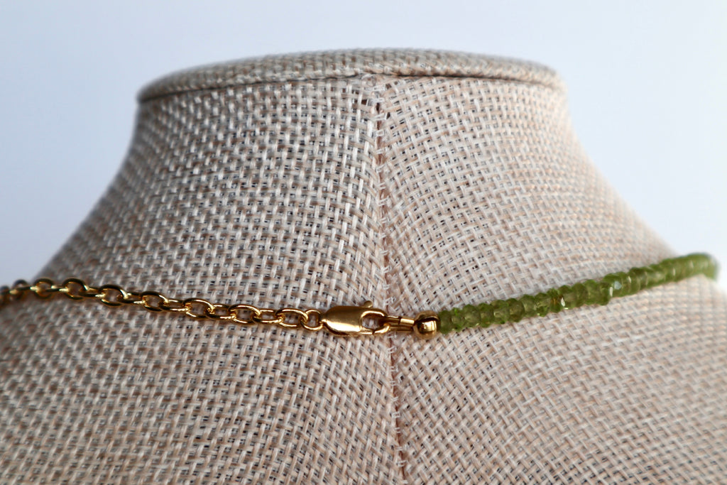 Close-up of the Florae necklace on a linen bust form showing the back of the piece, with the 14k gold-filled lobster clasp and the contrast between the gold cable chain and faceted peridot bead strand