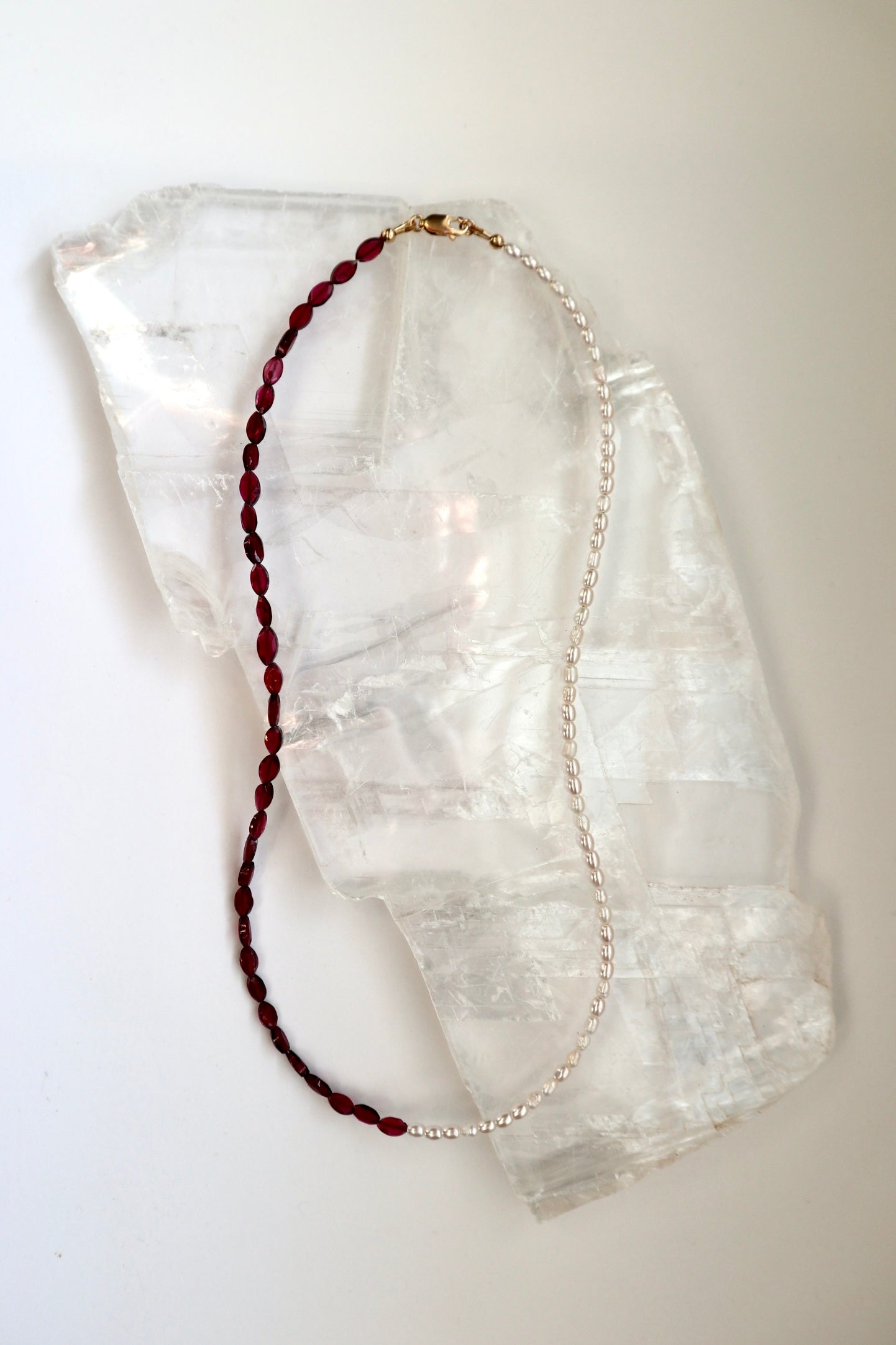 Garnelle necklace by Auréad Designs, featuring marquise garnet gemstone beads and freshwater pearls with a gold-filled clasp, laid flat on a white selenite slab