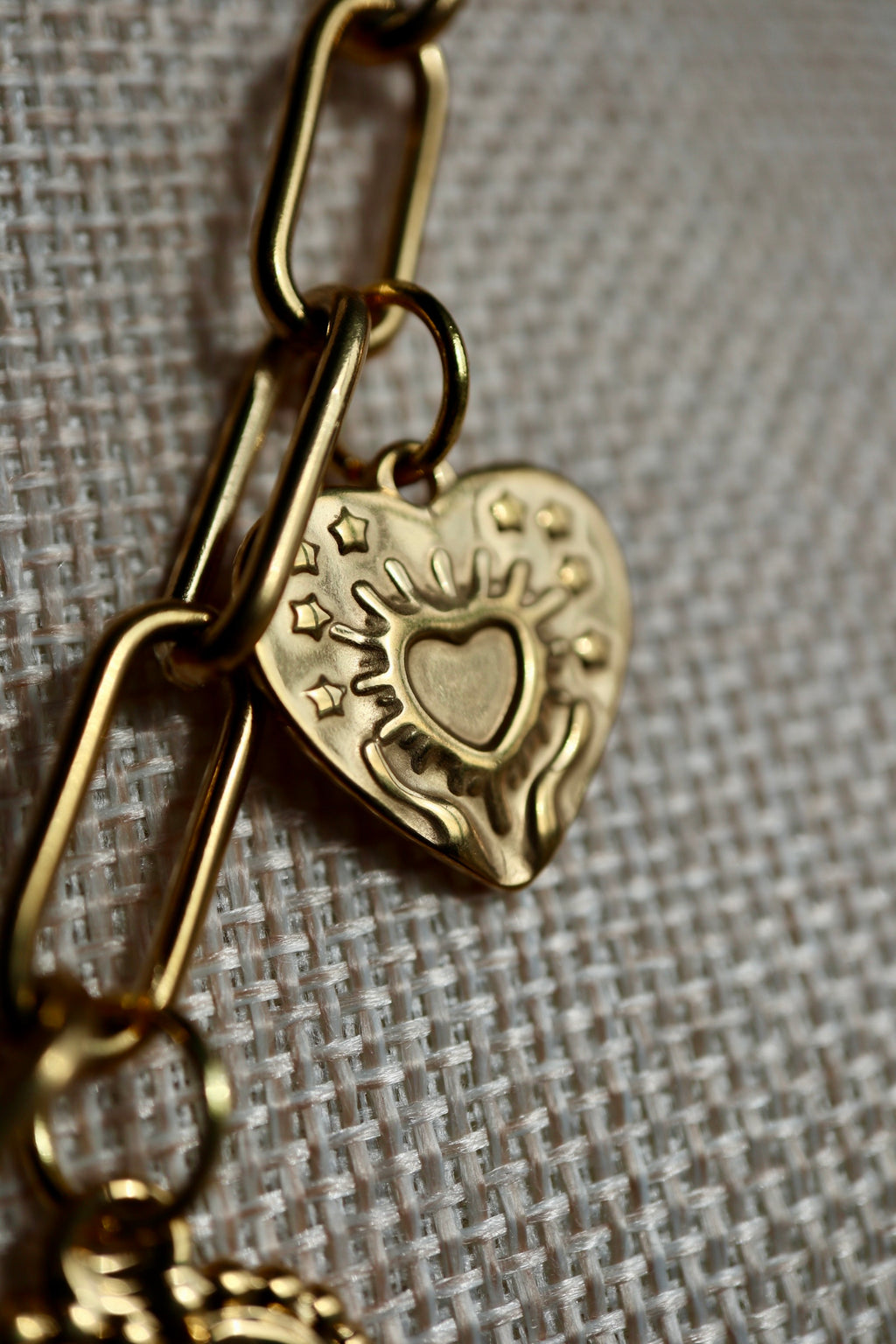 Macro close-up of the Heartstrong necklace on a linen bust form, showing an ornate gold stainless steel heart charm with an embossed inner heart, star accents, and decorative scrollwork detail