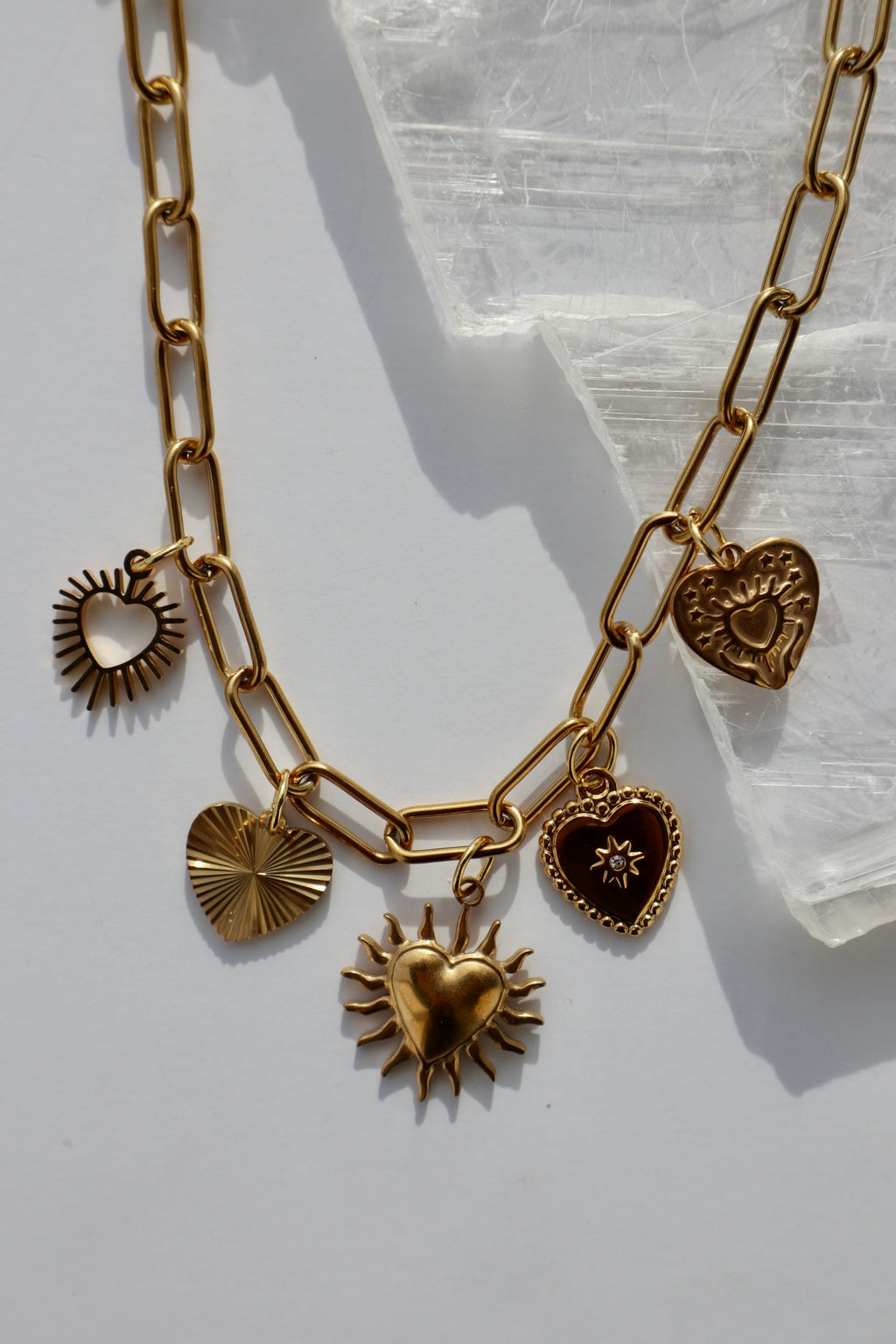 Close-up of the Heartstrong necklace showing five gold stainless steel heart charms suspended from a gold paperclip chain