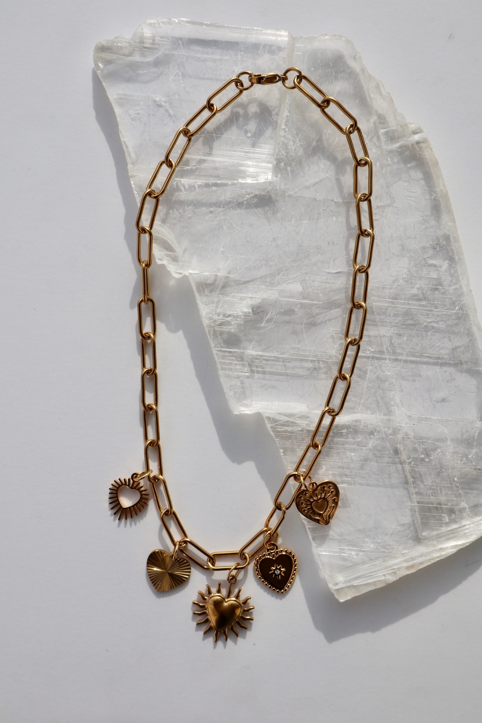 Heartstrong necklace by Auréad Designs, featuring a gold stainless steel paperclip chain with five freely moving gold heart charms and a lobster clasp, laid flat on a white selenite slab