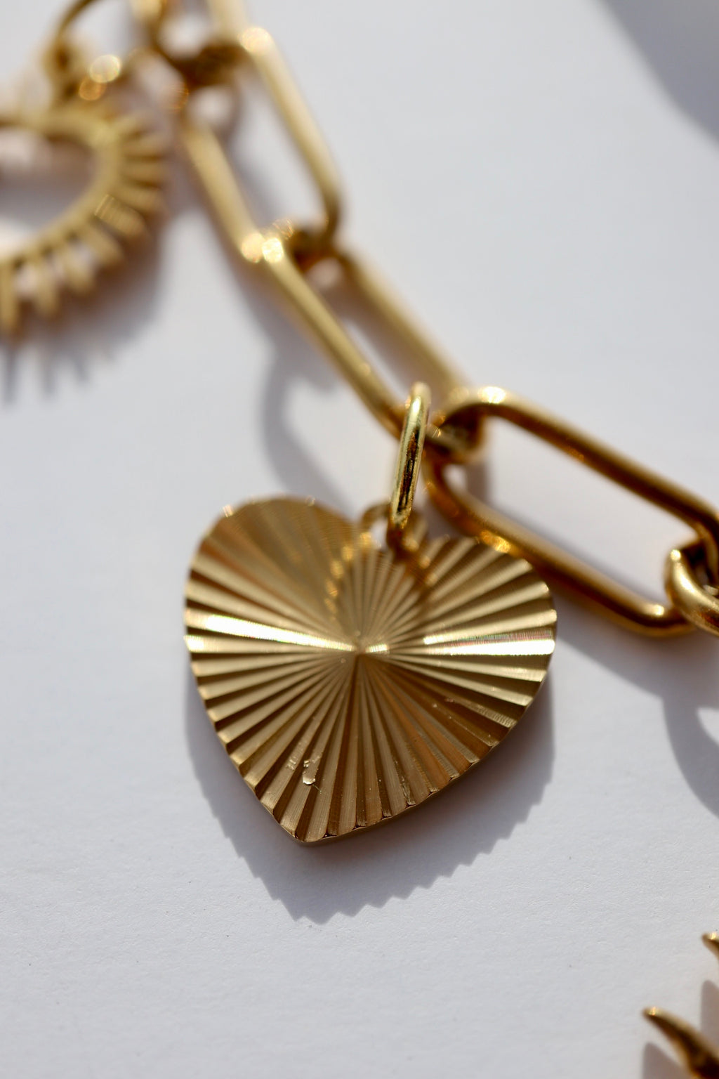 Macro close-up of the Heartstrong necklace by Auréad Designs showing a gold stainless steel ribbed sunburst-pattern heart charm suspended from a gold paperclip chain link