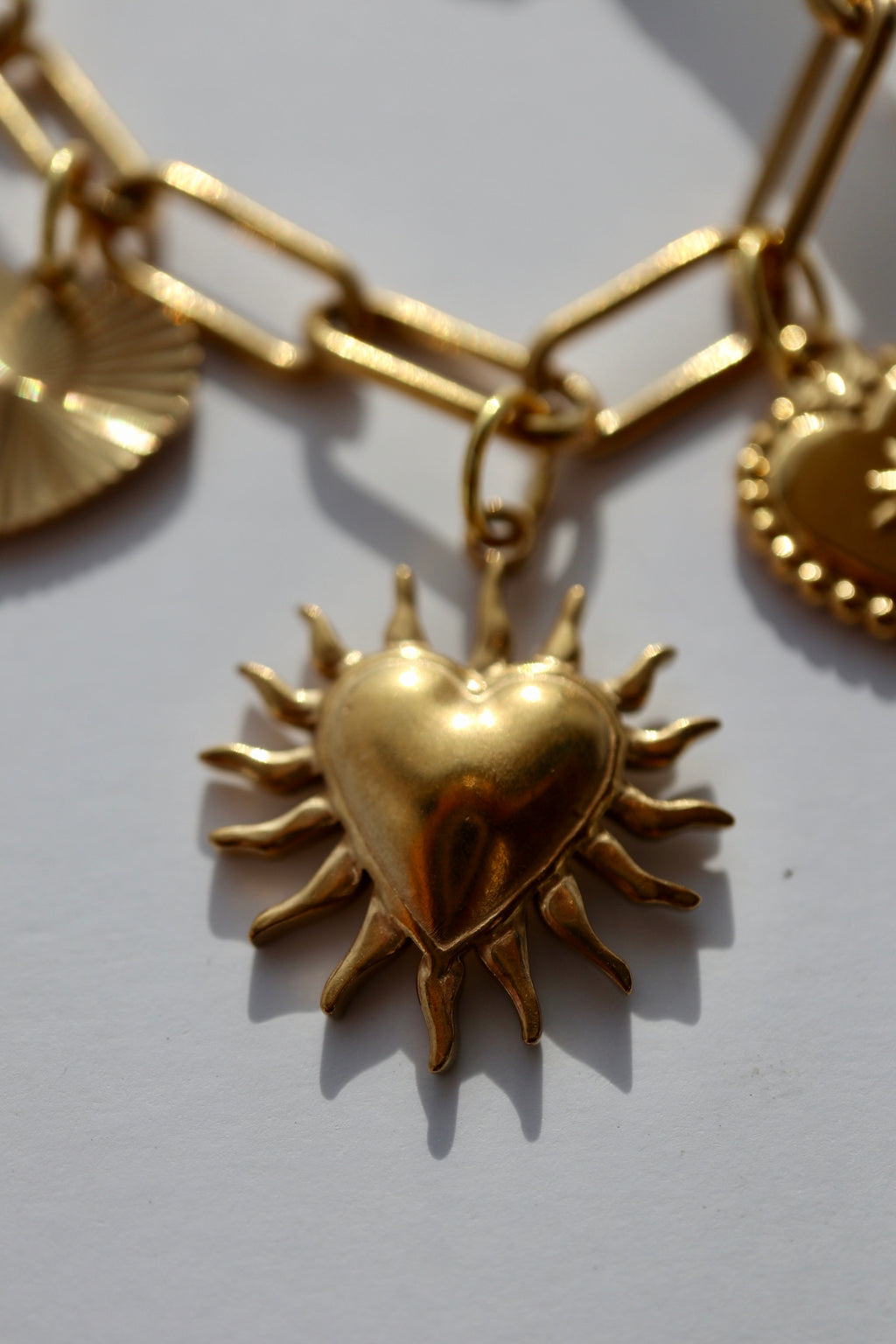 Macro close-up of the Heartstrong necklace by Auréad Designs highlighting the sculptural gold stainless steel sacred heart charm with radiating sunburst rays, suspended from the gold paperclip chain