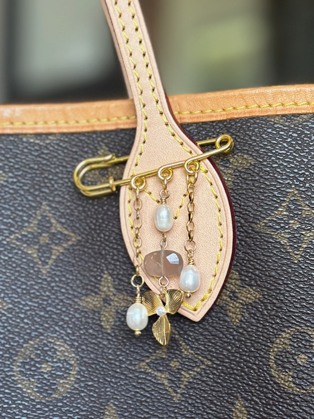 Auréad Designs Ilvara gold kilt pin brooch with peach moonstone and freshwater pearl drops pinned to a tan leather bag strap.