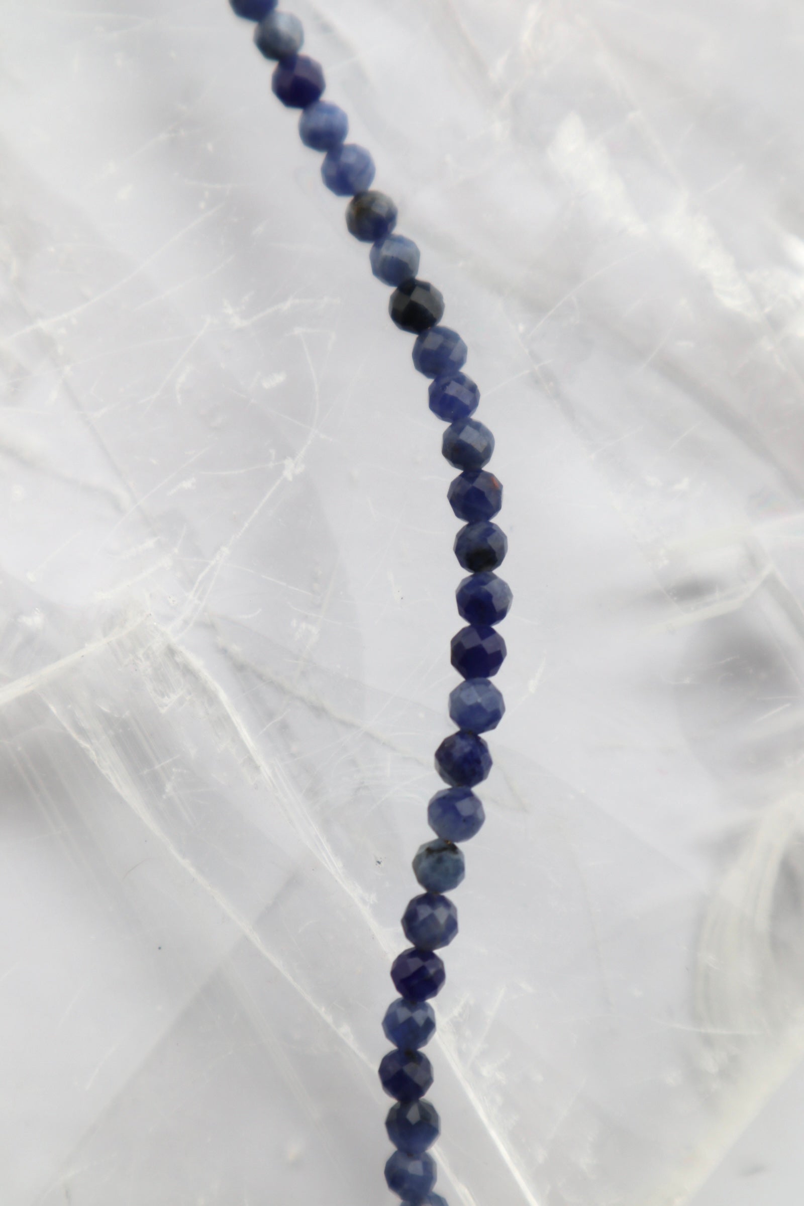 Close-up of the Indira necklace on a white selenite slab, showing the individual facets and natural deep blue tone variation of the sodalite gemstone beads