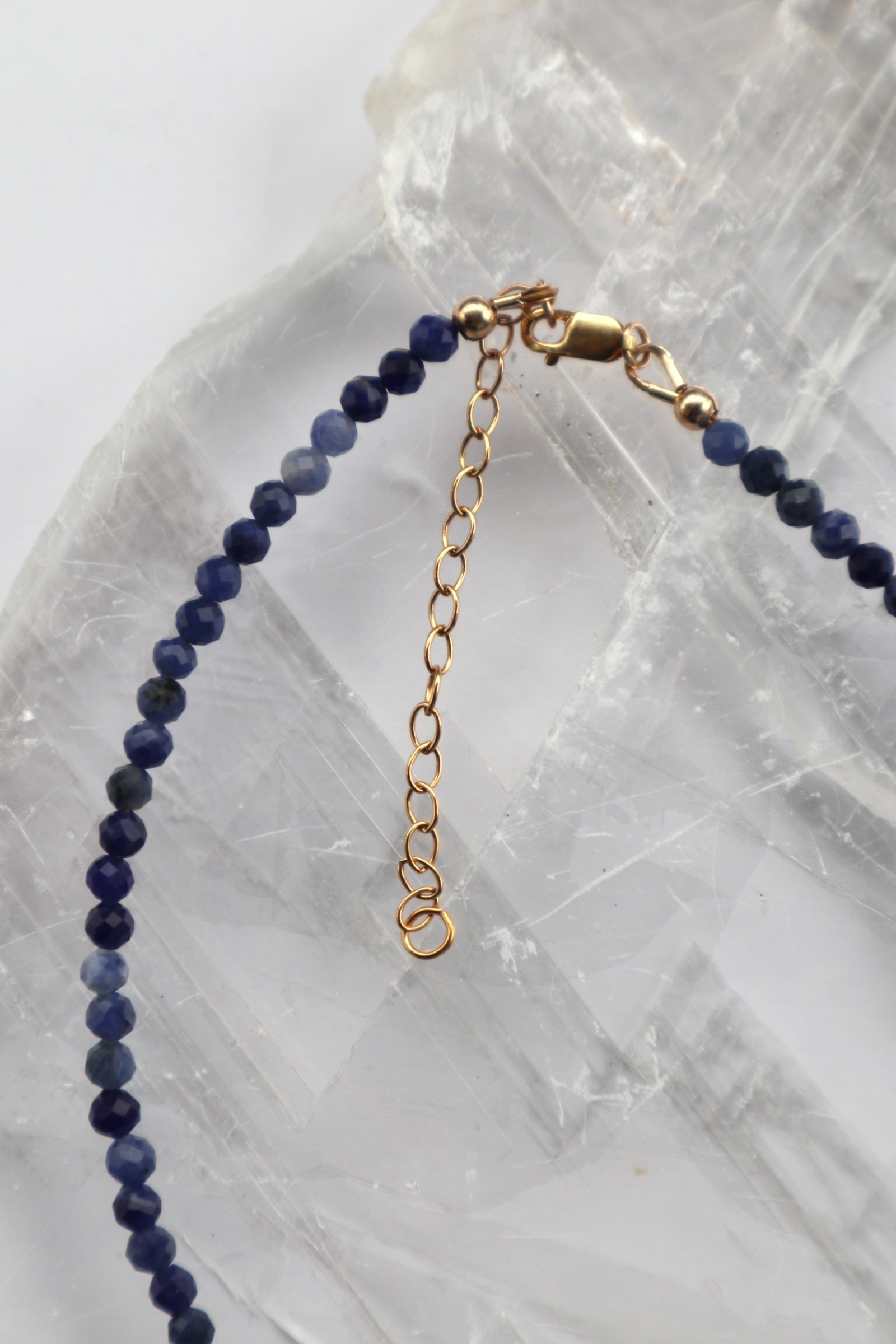 Detail shot of the Indira necklace showing the 14k gold-filled clasp and two-inch extender chain alongside the faceted deep blue sodalite beads