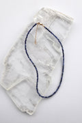  Indira necklace by Auréad Designs, featuring small faceted sodalite gemstone beads in deep blue with a 14k gold-filled clasp and extender chain, laid flat on a white selenite slab