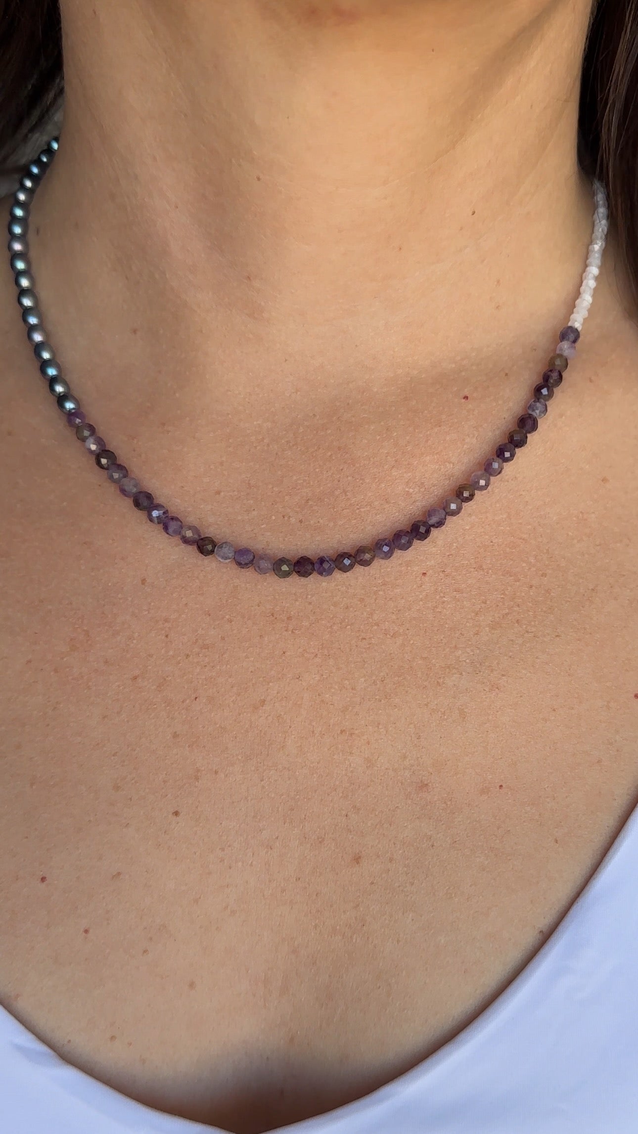 Auréad Designs Irisenne necklace with peacock green freshwater pearls and faceted amethyst beads worn across the collarbone and chest over a white top, showing full drape and length.