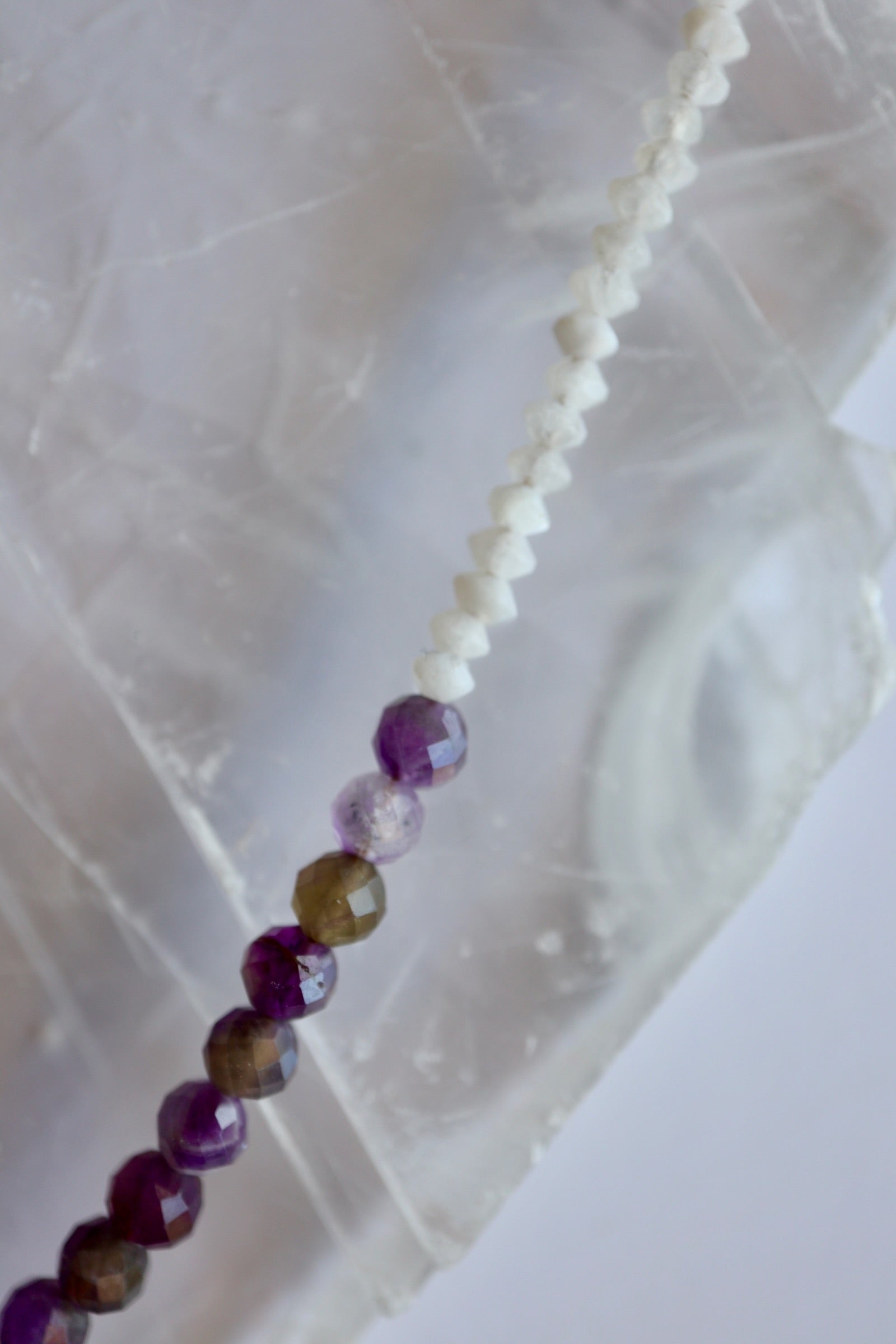 Macro detail of Auréad Designs Irisenne necklace showing faceted rainbow moonstone rondelles transitioning into amethyst beads on white selenite slab.