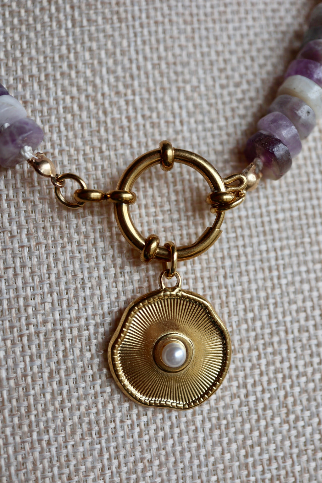 Close-up of the Isolde necklace showing the removable gold stainless steel freshwater pearl pendant and sailor spring clasp alongside amethyst heishi beads on a cream silk-knotted strand