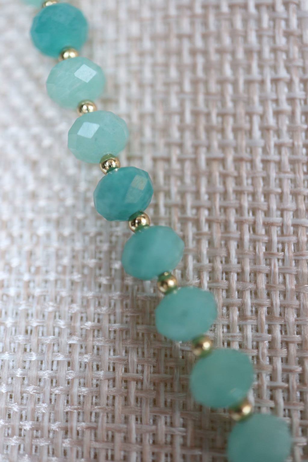 Close-up of faceted amazonite rondelles on the Lake necklace by Auréad Designs, showing the vivid turquoise-green color and gold spacer beads between each stone