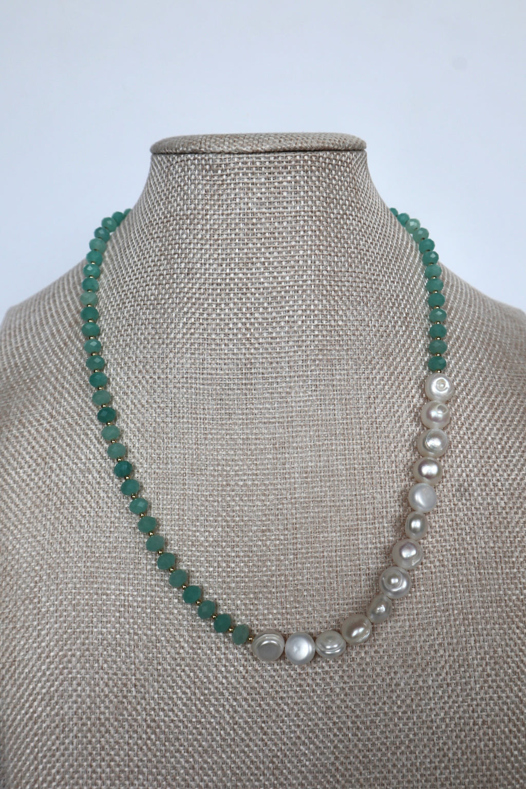 Lake necklace by Auréad Designs displayed on a linen bust, front view showing the asymmetric design with amazonite rondelles on one side and large coin freshwater pearls on the other, Glacier Collection