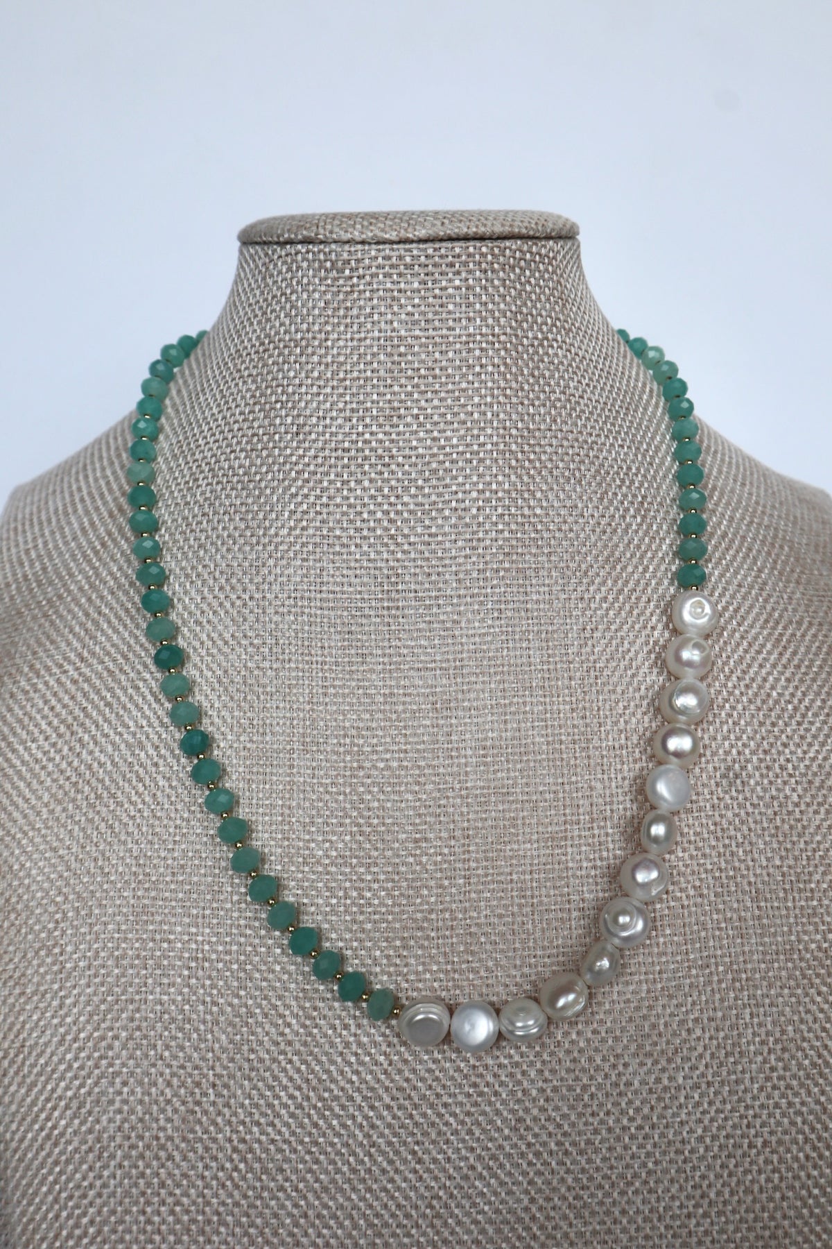 Lake necklace by Auréad Designs displayed on a linen bust, front view showing the asymmetric design with amazonite rondelles on one side and large coin freshwater pearls on the other, Glacier Collection