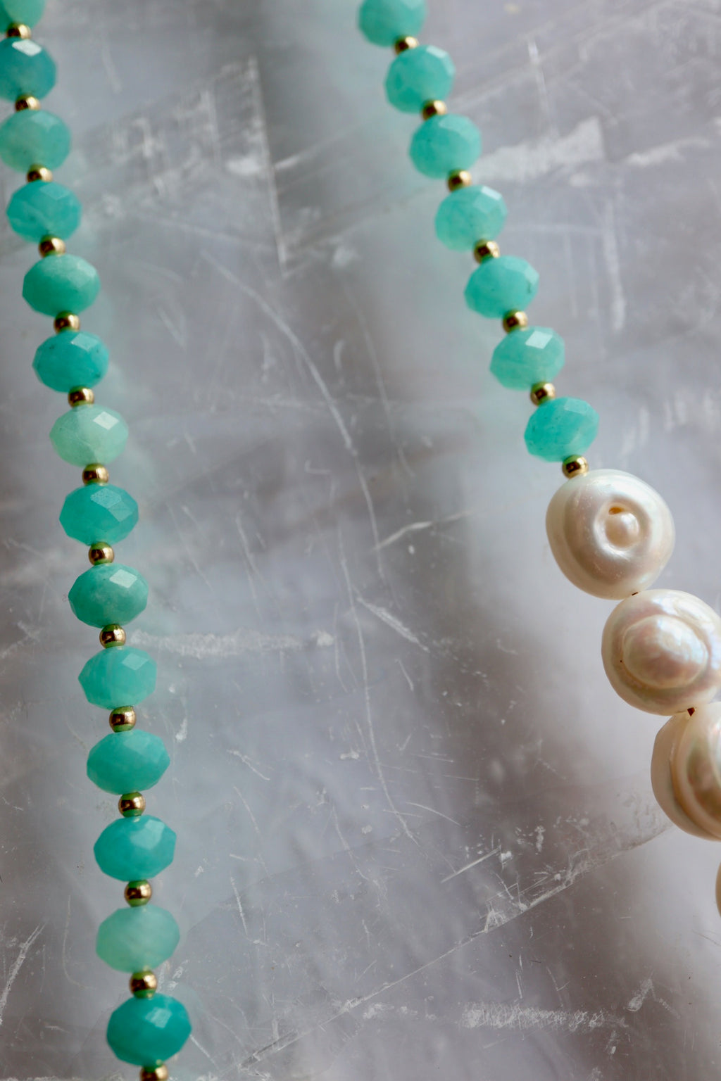 Detail shot of the Lake necklace by Auréad Designs on a selenite slab, showing the transition from faceted amazonite rondelles to large coin freshwater pearls