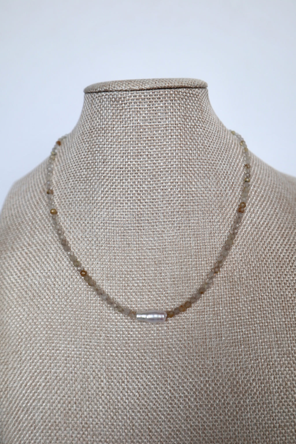 Larch necklace by Auréad Designs displayed on a linen bust, front view of the full golden rutilated quartz strand with single baroque freshwater pearl focal bead centered, Glacier Collection