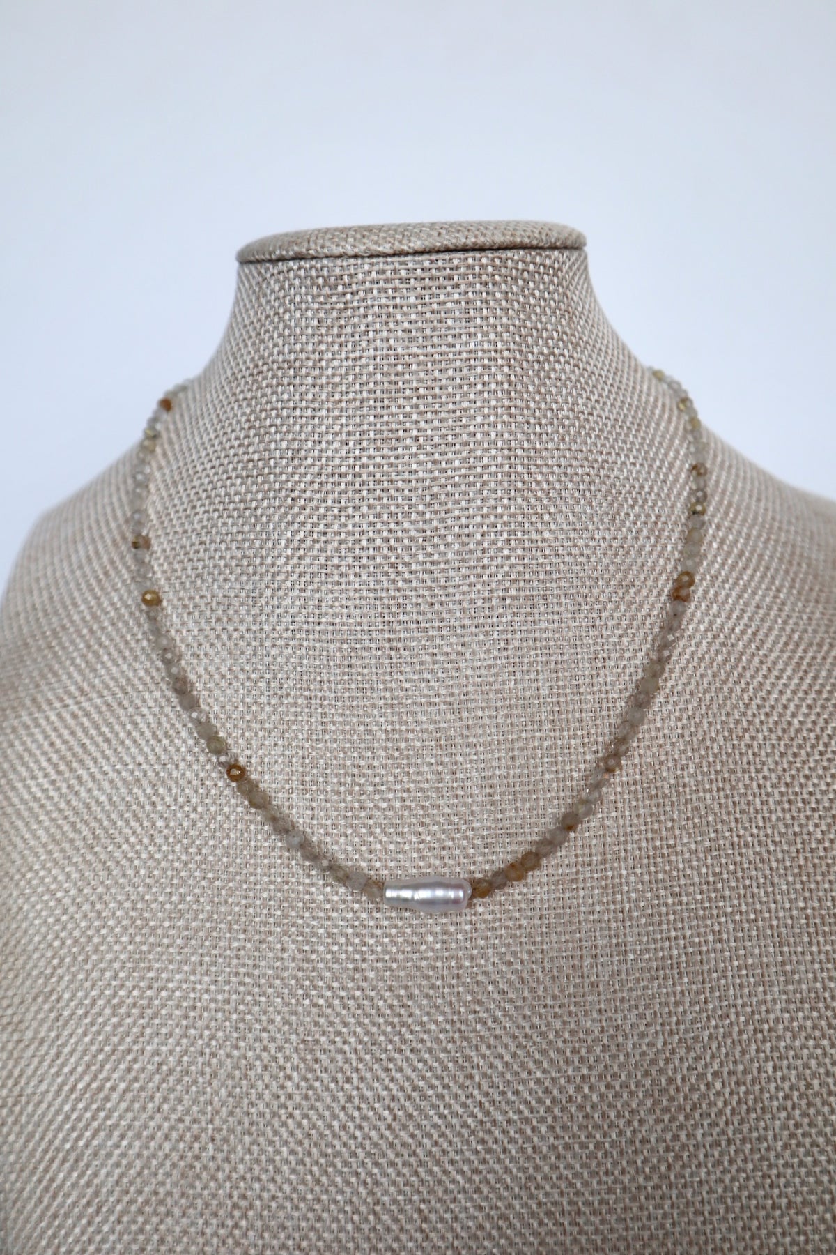 Larch necklace by Auréad Designs displayed on a linen bust, front view of the full golden rutilated quartz strand with single baroque freshwater pearl focal bead centered, Glacier Collection