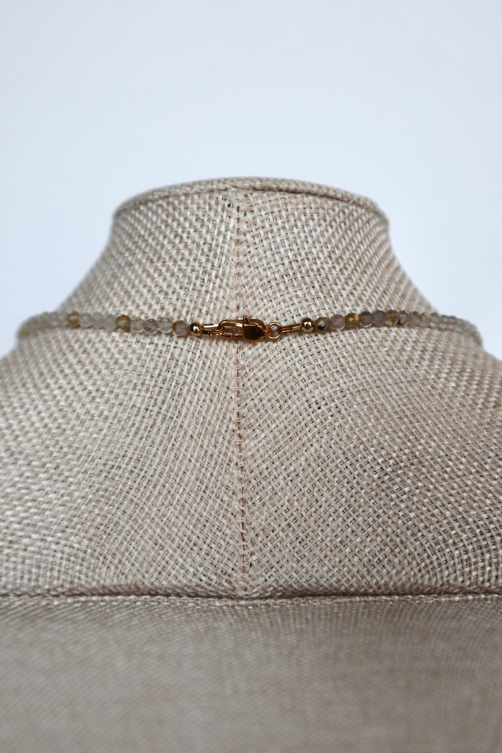 Close-up of the gold lobster clasp on the Larch necklace by Auréad Designs, with golden rutilated quartz beads on either side