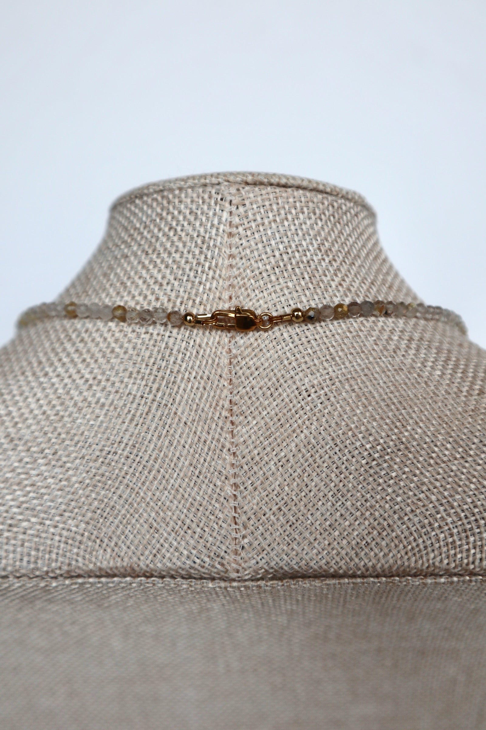 Close-up of the gold lobster clasp on the Larch necklace by Auréad Designs, with golden rutilated quartz beads on either side
