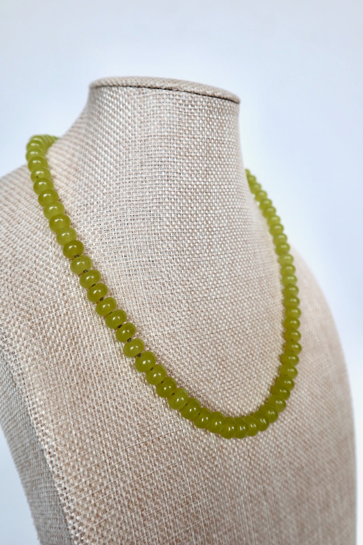 Ledge necklace by Auréad Designs on a linen bust, angled view showing the full silk-knotted lemon jade rondelle strand and gold toggle clasp