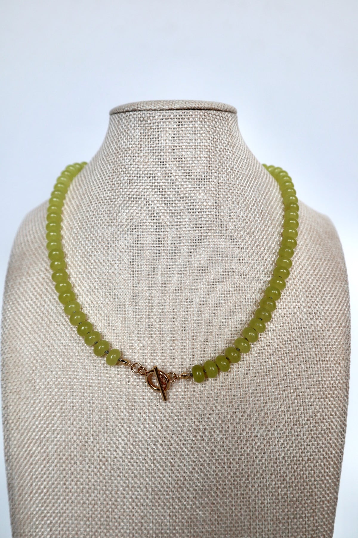 Ledge necklace by Auréad Designs displayed on a linen bust, front view of the full lemon jade rondelle strand with gold toggle clasp, Glacier Collection