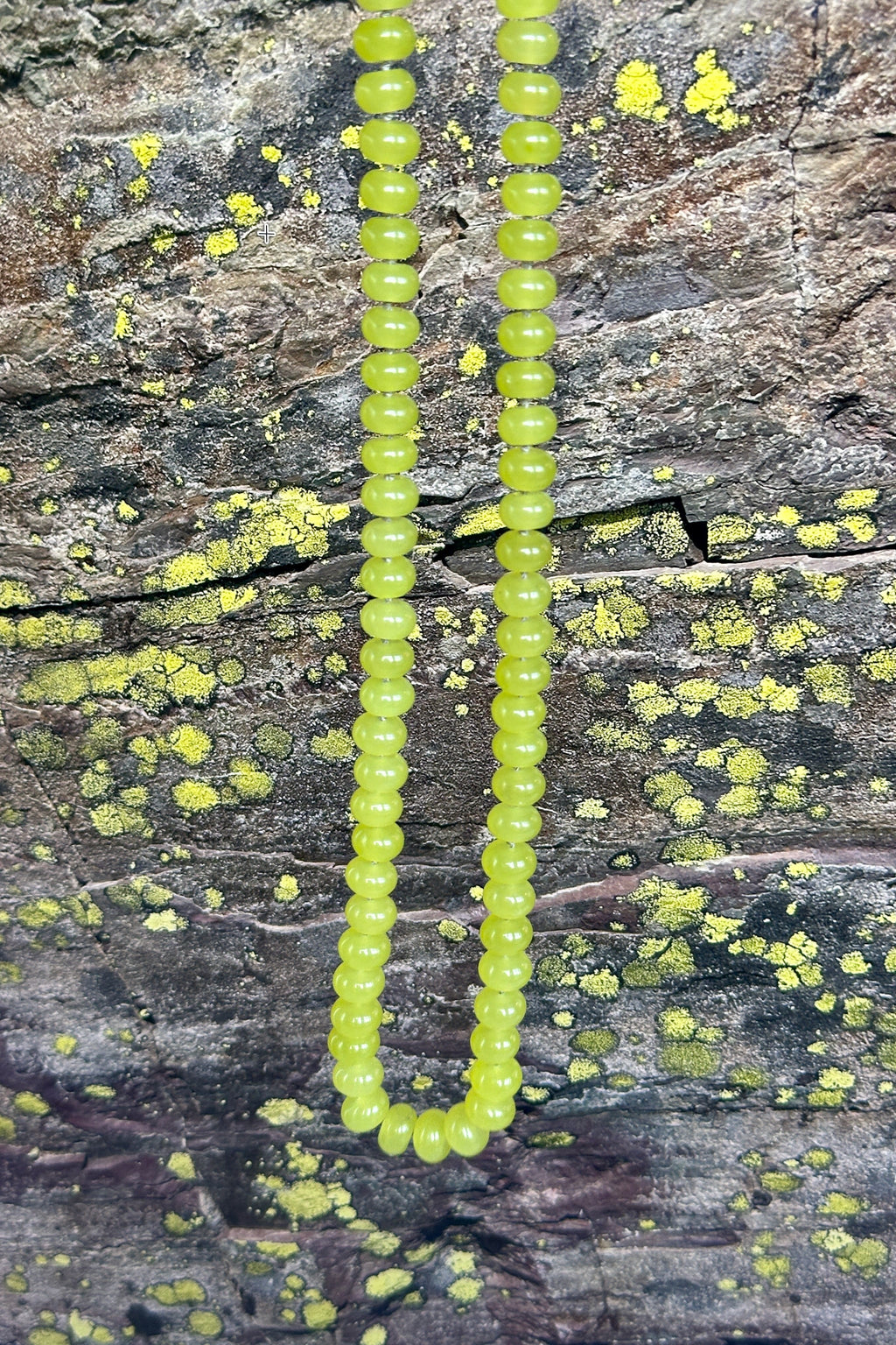 Ledge necklace by Auréad Designs laid on lichen-covered rock, showing the vivid yellow-green of the lemon jade beads against bright lichen and gray shale, the landscape that inspired the piece, from the Glacier Collection