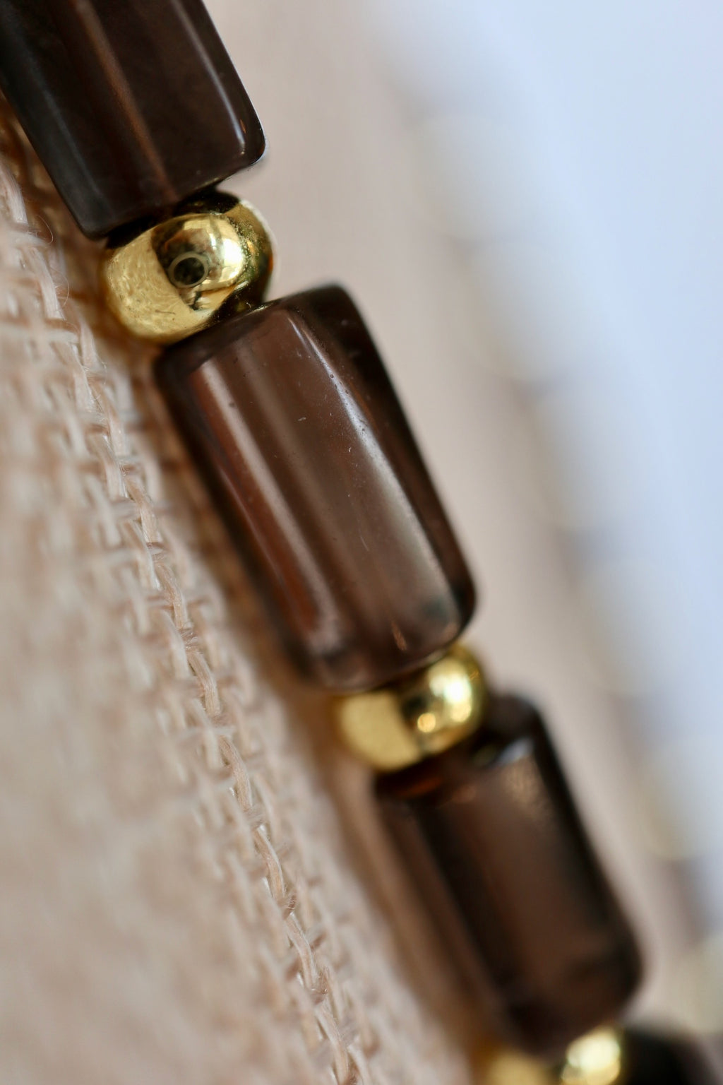 Auréad Designs Leoven necklace close-up of faceted smoky quartz cylinder beads and gold stainless steel spacers on linen bust form, showing warm translucent brown tones of the stone