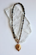 Auréad Designs Leoven necklace laid flat on white selenite slab, showing full strand of faceted smoky quartz cylinder beads with gold spacers, spring ring clasp, and gold lion head pendant with CZ eyes