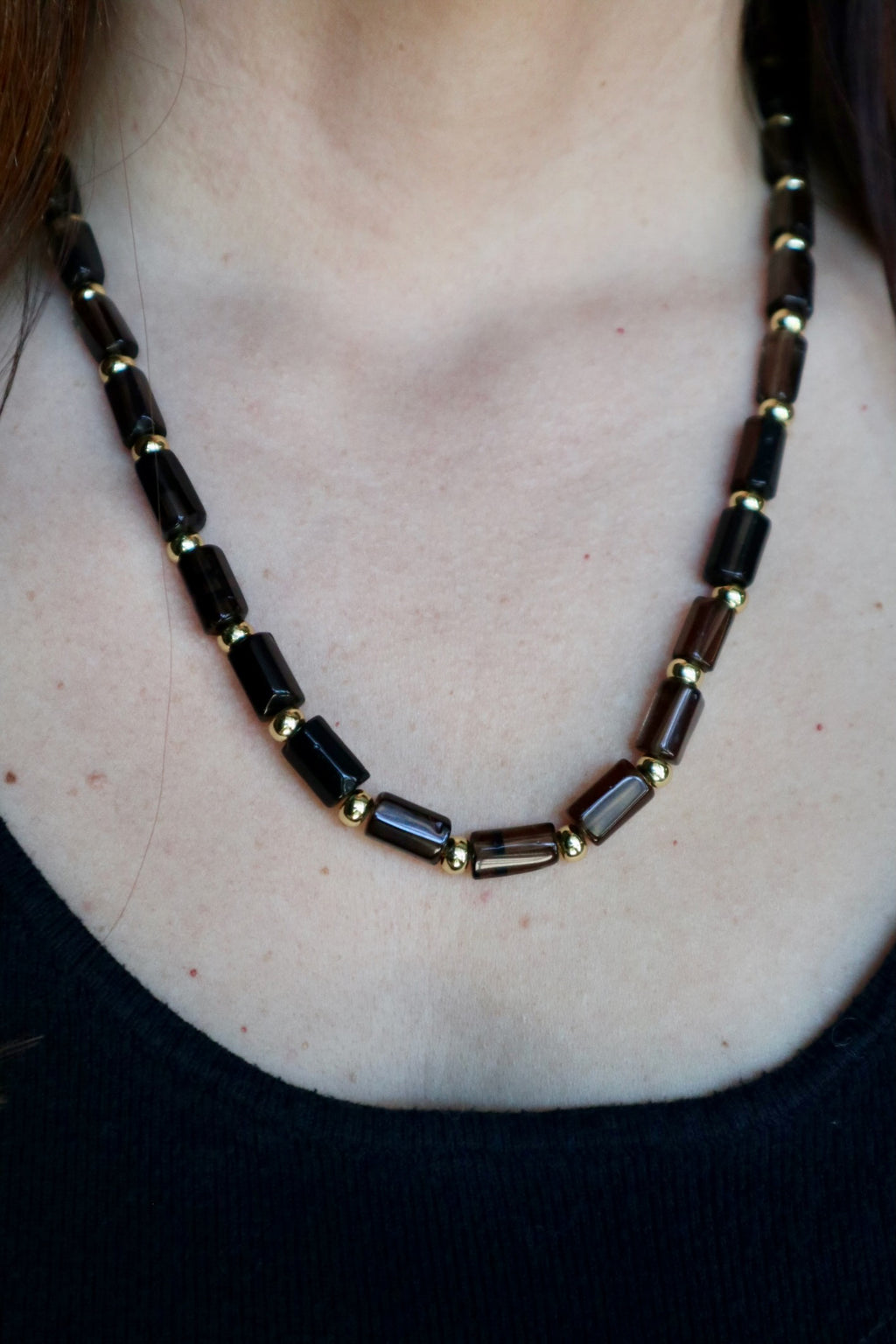 Auréad Designs Leoven necklace worn without the lion pendant on a black ribbed top, showing the clean beaded silhouette of smoky quartz cylinder beads and gold spacers at collarbone length