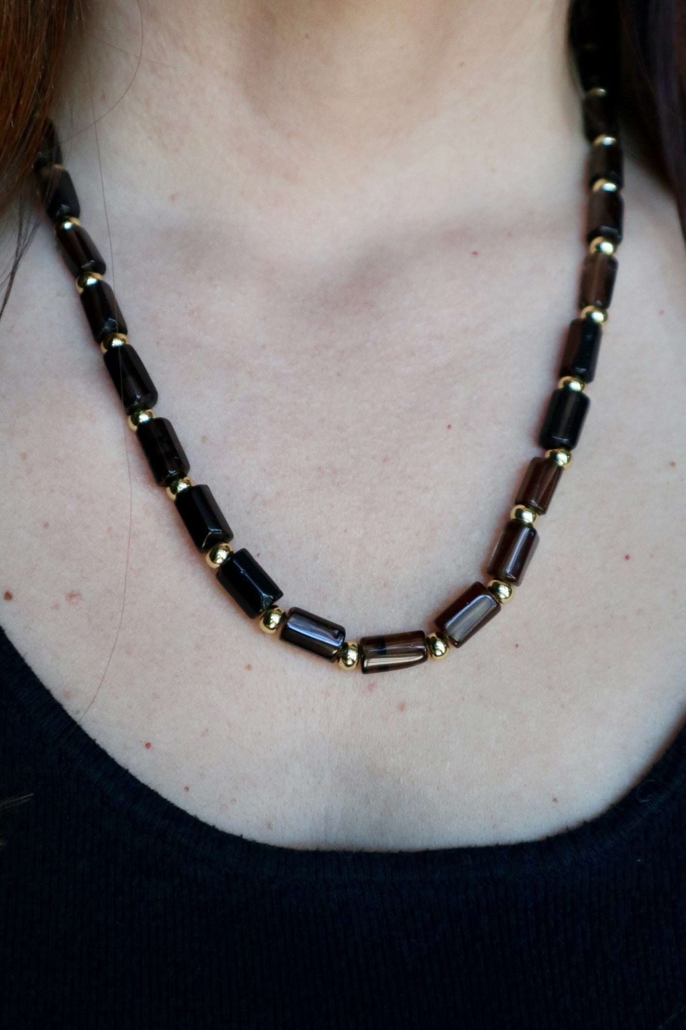 Auréad Designs Leoven necklace worn without the lion pendant on a black ribbed top, showing the clean beaded silhouette of smoky quartz cylinder beads and gold spacers at collarbone length