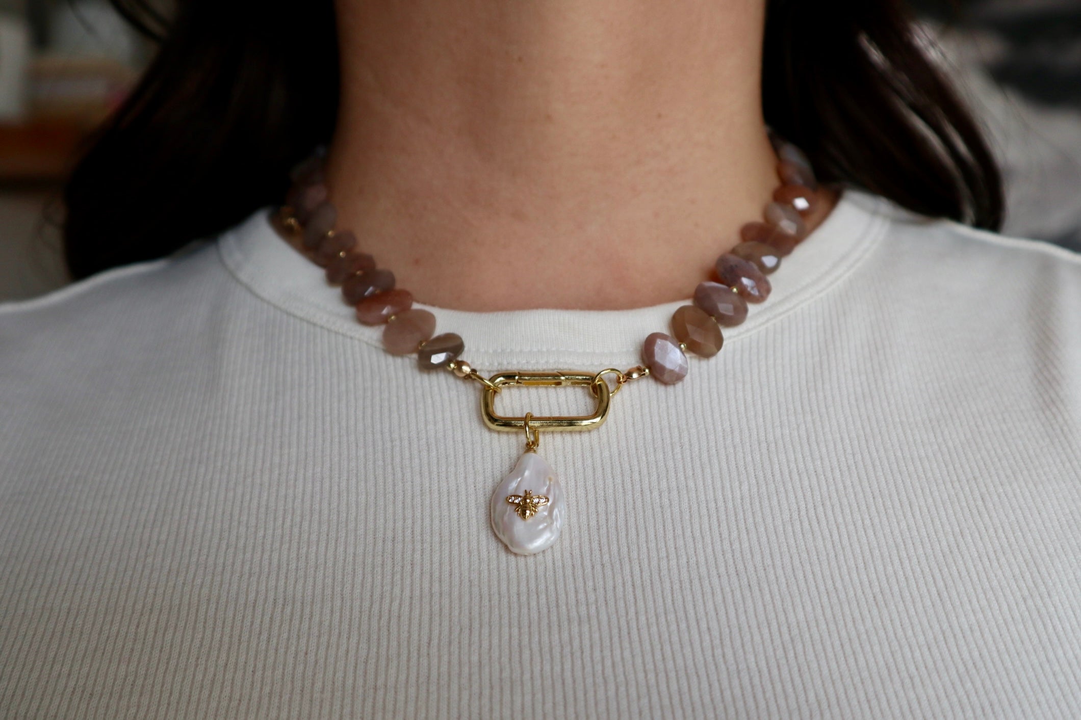 Lucent peach moonstone necklace worn at the collarbone with the gold-filled carabiner clasp centered at the front as a styling focal point, styled with a white top