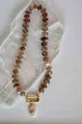 Lucent necklace by Auréad Designs, featuring peach moonstone gemstone beads, gold-filled spacer beads, a gold-filled carabiner clasp, and a removable freshwater pearl charm, laid flat on a white selenite slab