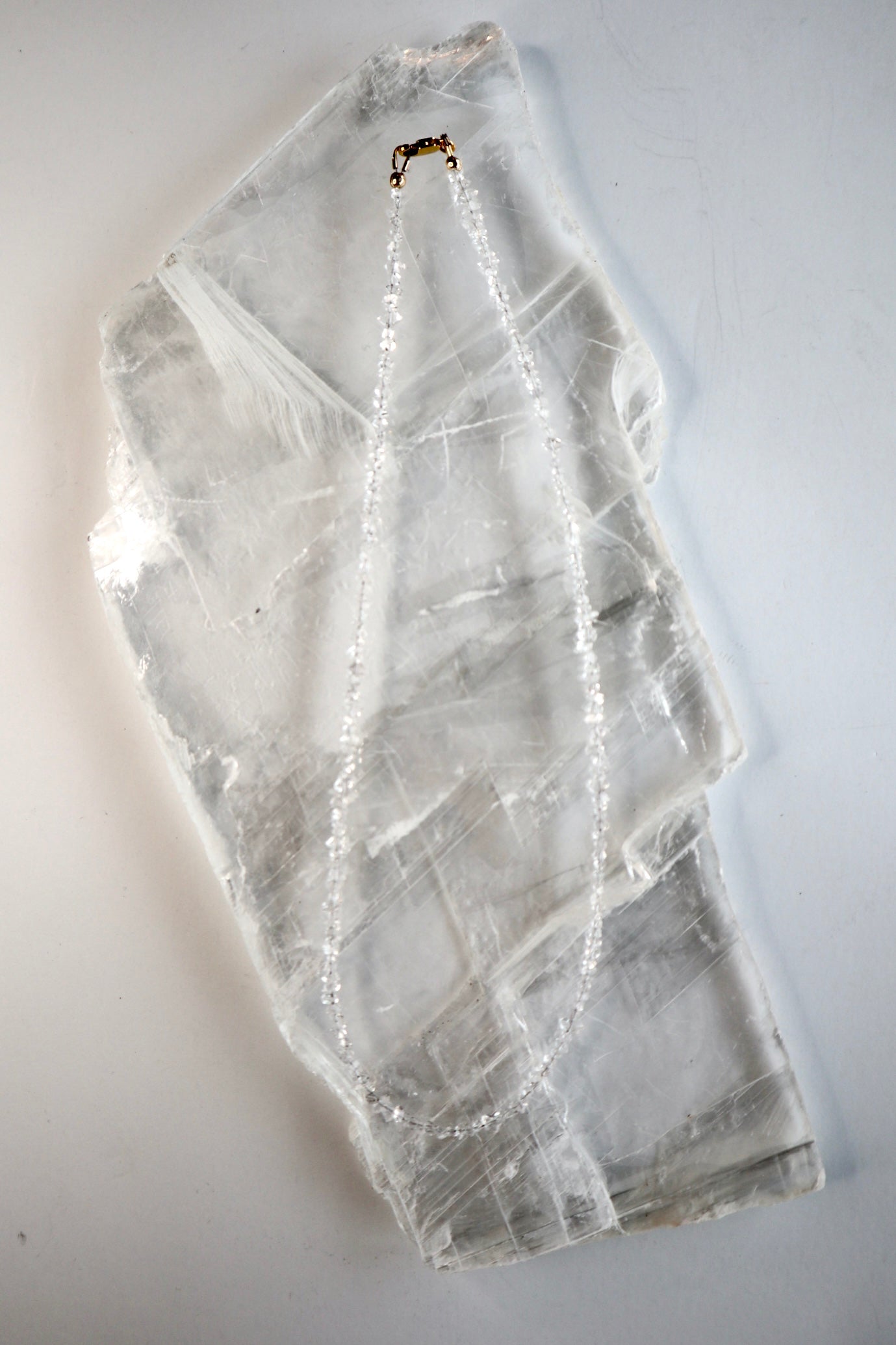 Lumenne herkimer diamond chip necklace by Auréád Designs laid flat on a white selenite slab, showing the full 16-inch strand of icy faceted crystals with 14k gold-filled clasp