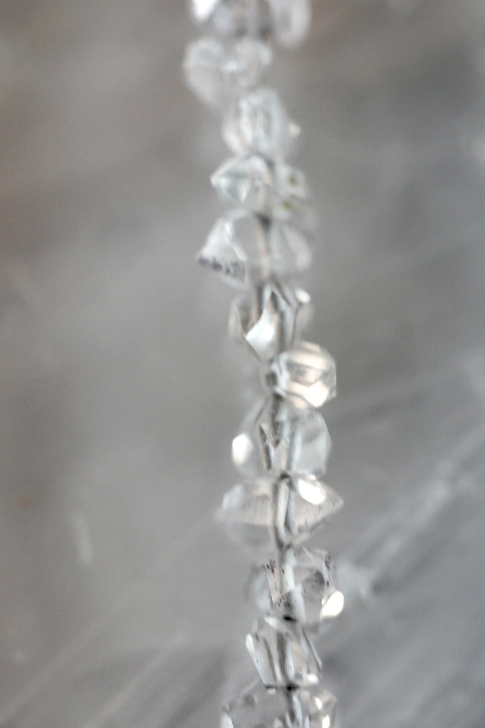 Close-up detail of the Lumenne necklace by Auréád Designs, showing the faceted herkimer diamond chips catching light against a soft grey background