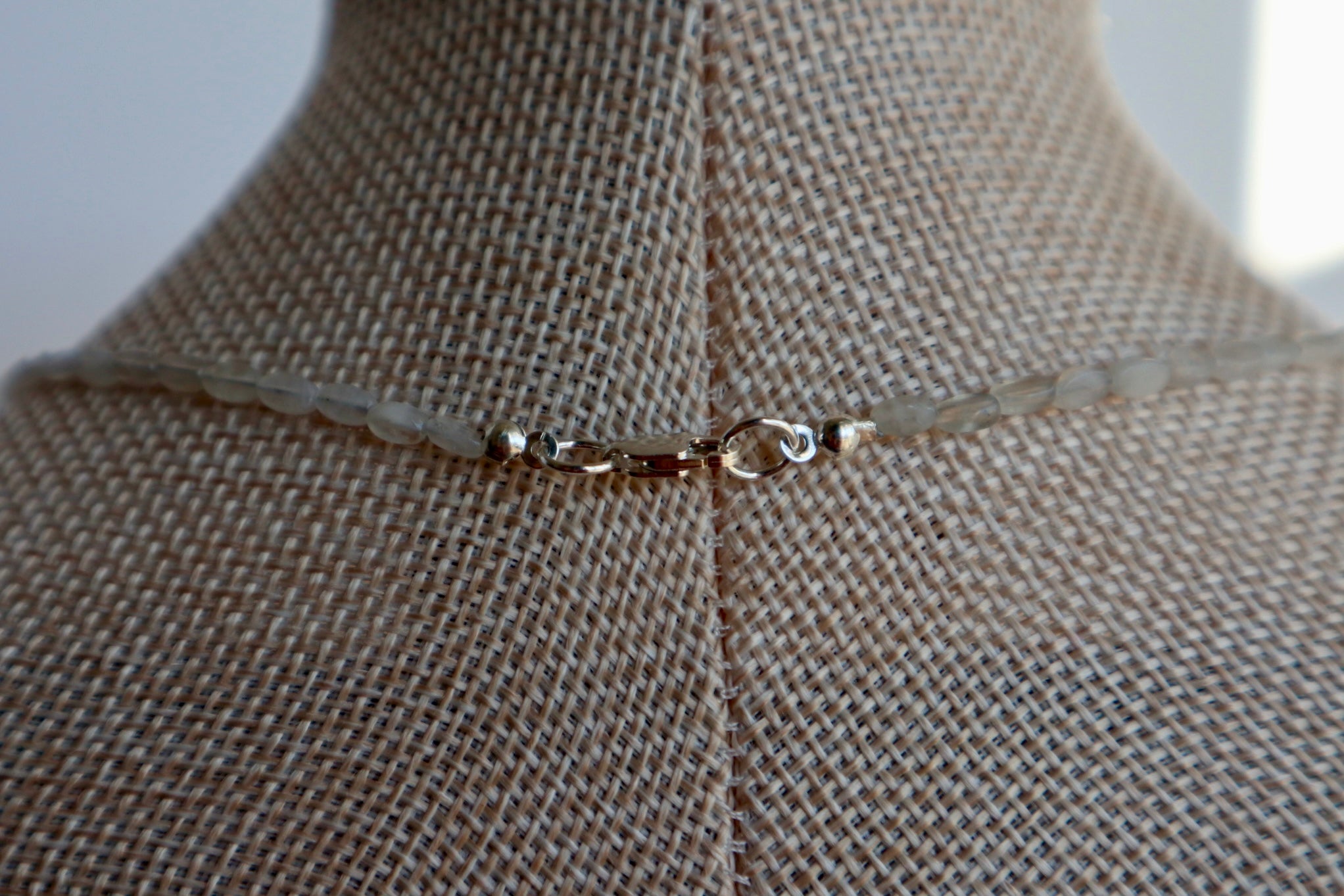 Close-up of the Lunamar necklace on a linen bust form, showing the sterling silver lobster clasp at the back and the delicate moonstone bead strand on either side