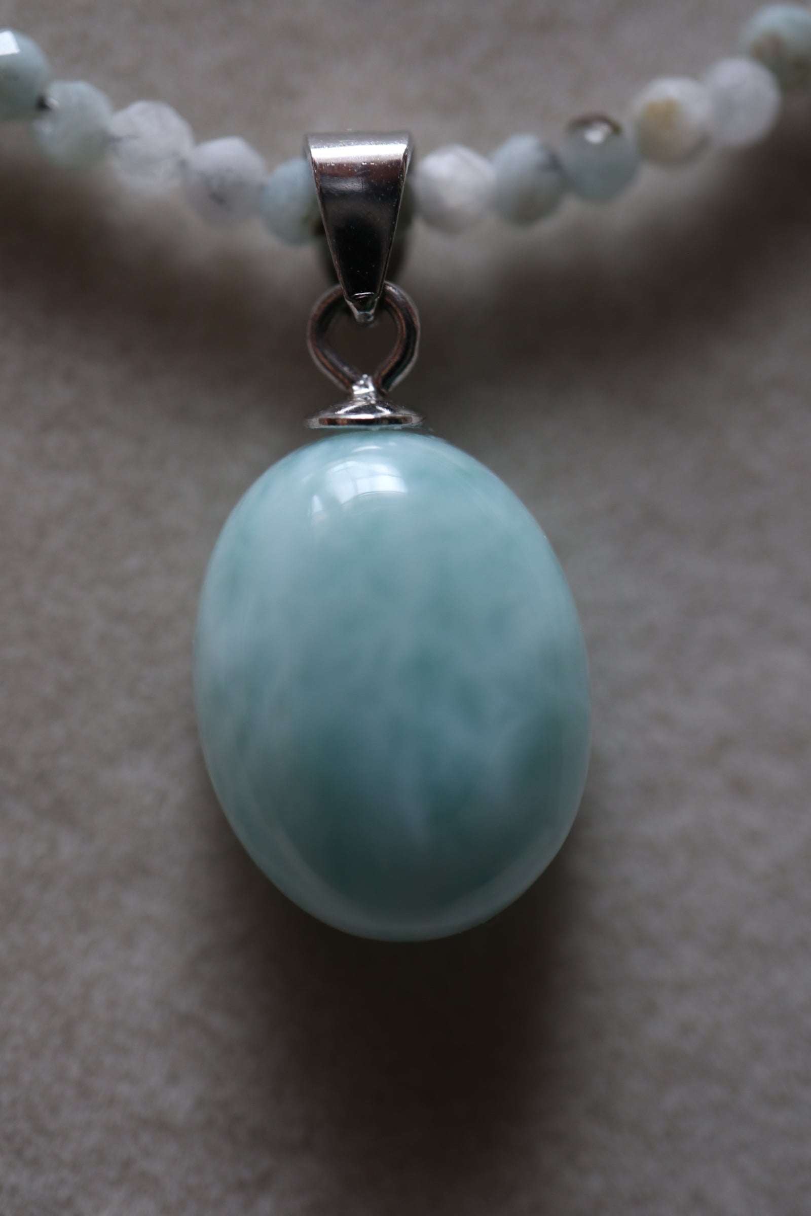 Macro close-up of the Lunamar necklace larimar pendant by Auréad Designs, showing the smooth oval larimar stone with its natural soft blue and white patterning suspended from a sterling silver bail