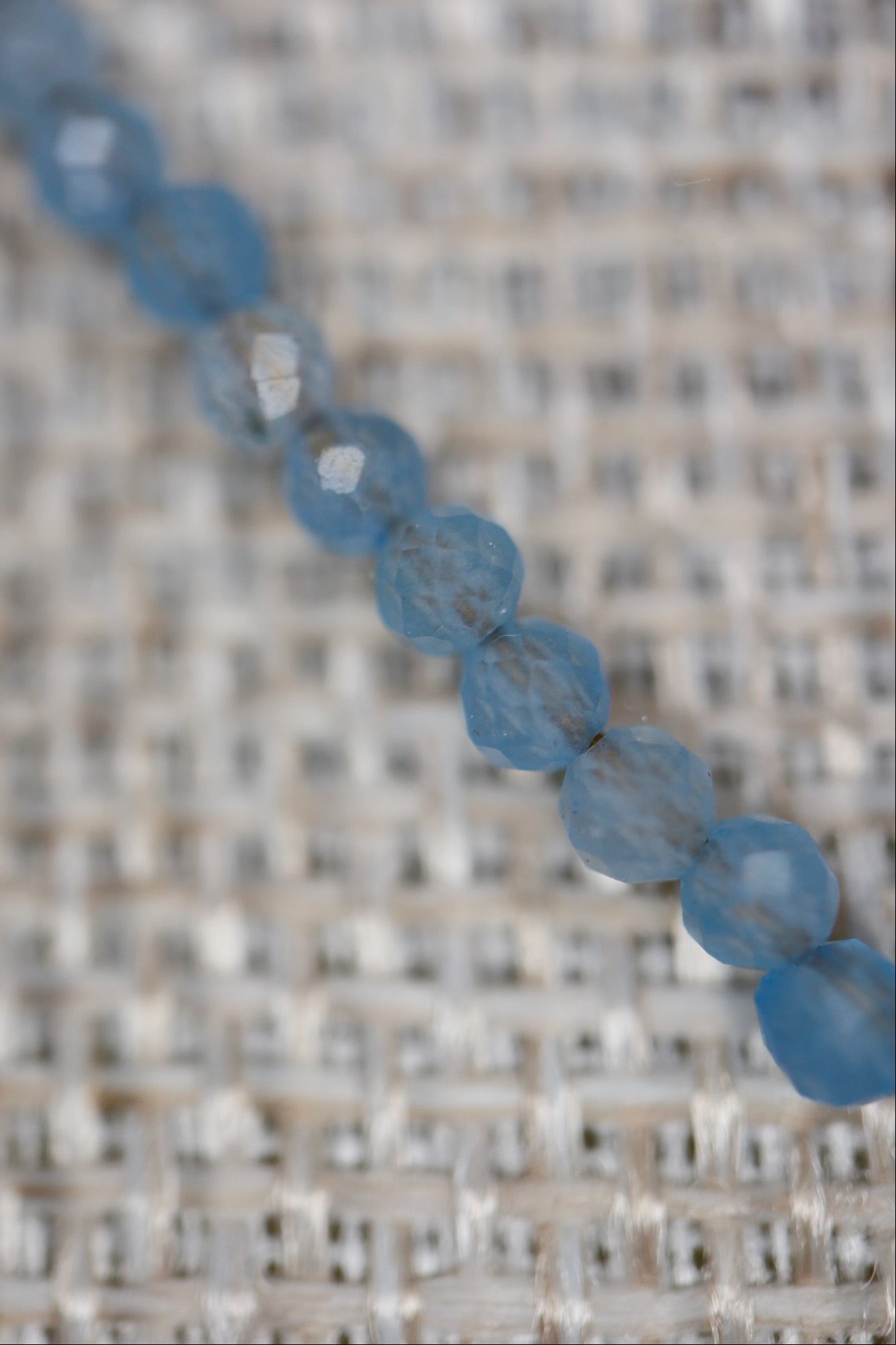 Macro detail of Auréad Designs Marevane faceted aquamarine beads on a linen bust form, showing bead texture and soft blue color.