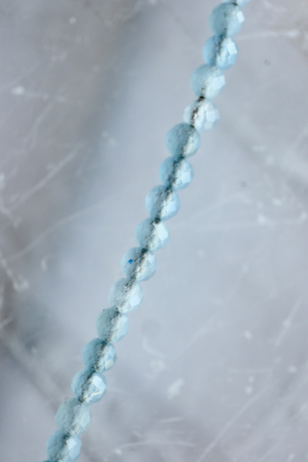 Macro detail of Auréad Designs Marevane necklace showing faceted natural aquamarine beads on white selenite slab.