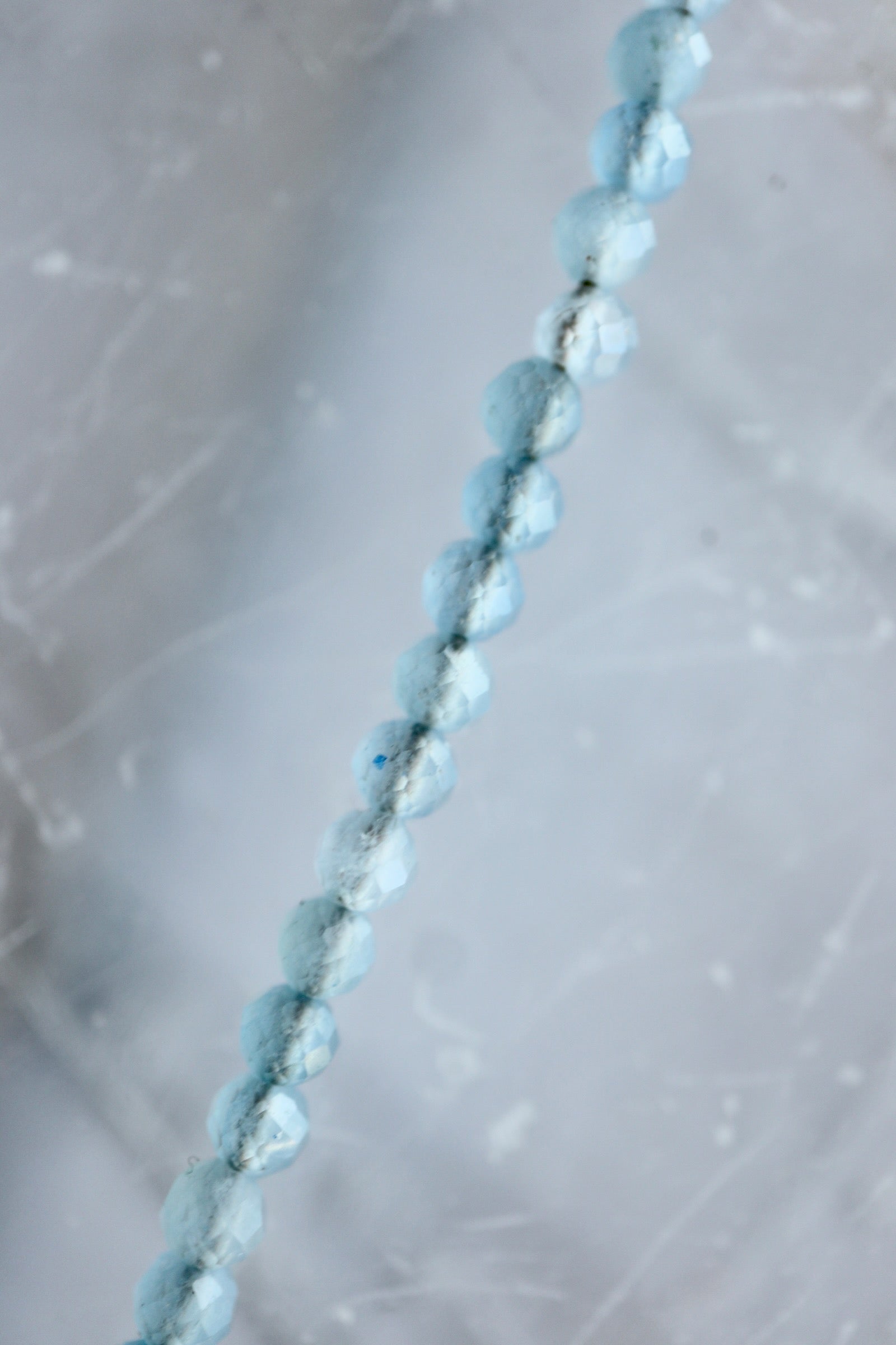 Macro detail of Auréad Designs Marevane necklace showing faceted natural aquamarine beads on white selenite slab.