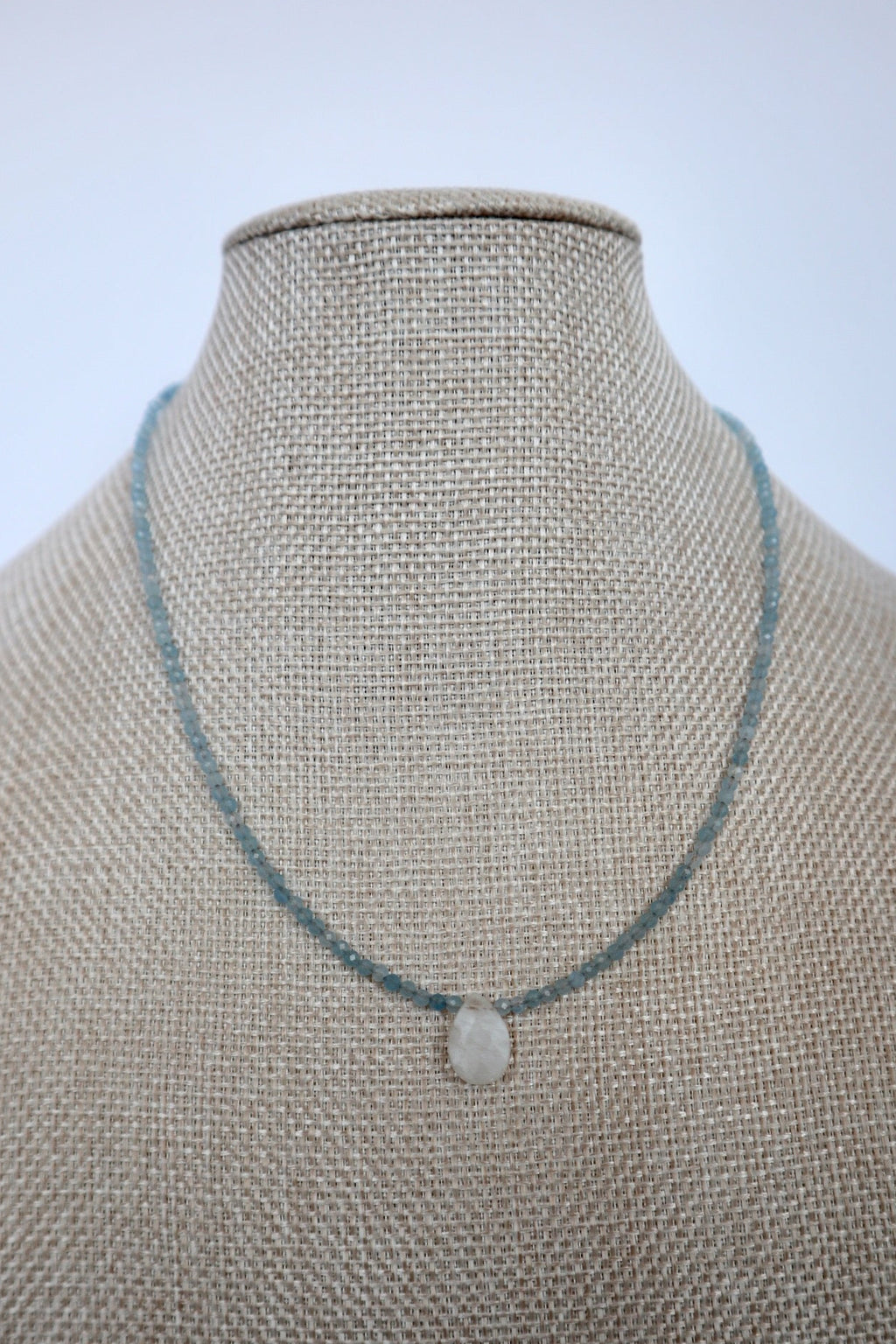 Auréad Designs Marevane aquamarine beaded necklace with rainbow moonstone teardrop pendant displayed on a linen bust form, front view.
