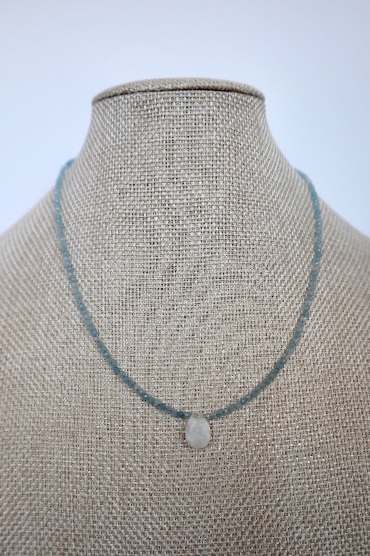 Auréad Designs Marevane aquamarine beaded necklace with rainbow moonstone teardrop pendant displayed on a linen bust form, front view.