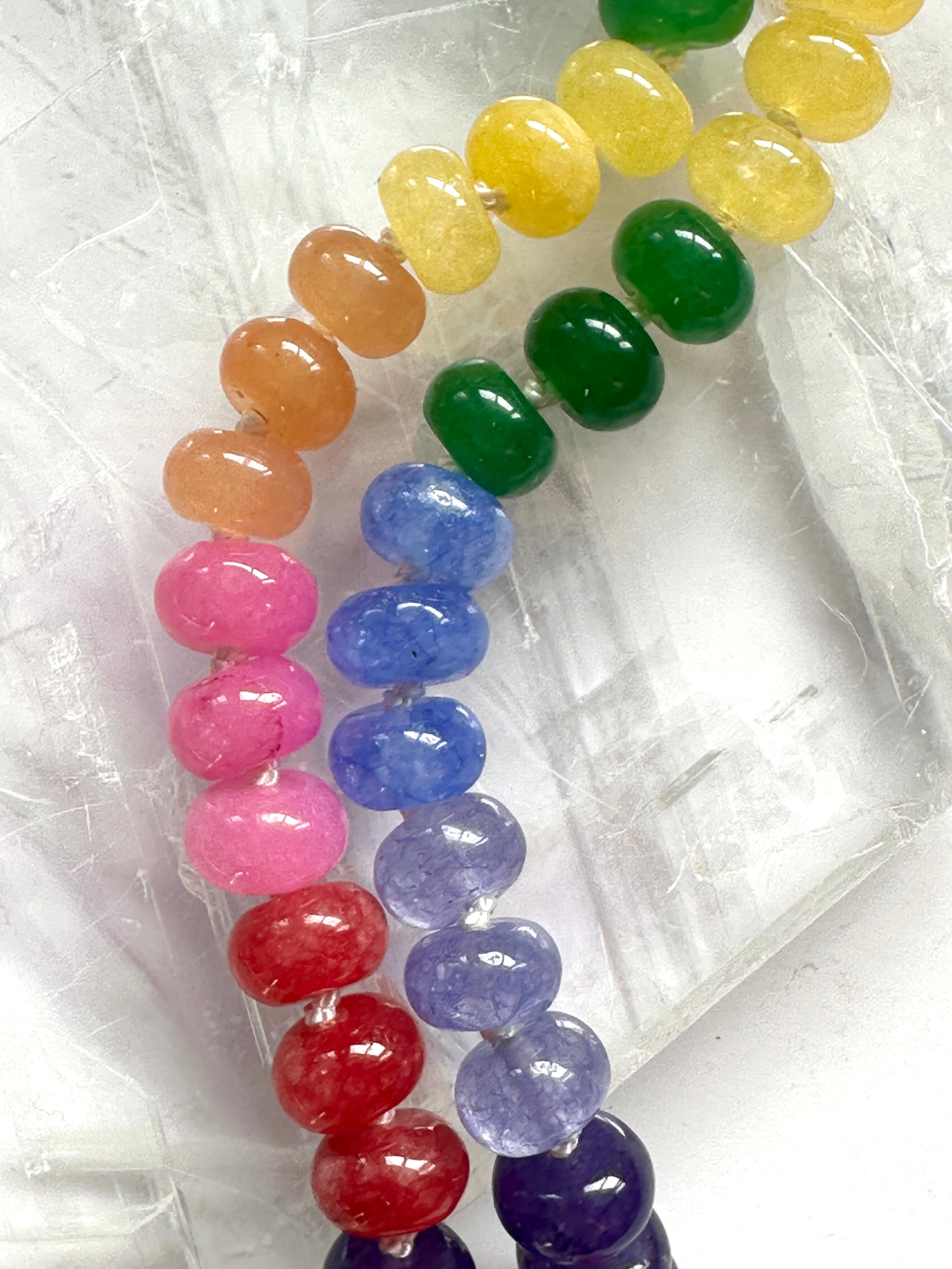 Close-up of the Maribelle necklace on a white selenite slab, showcasing the full rainbow spectrum of dyed candy jade beads including yellow, orange, pink, red, green, blue, and purple tones