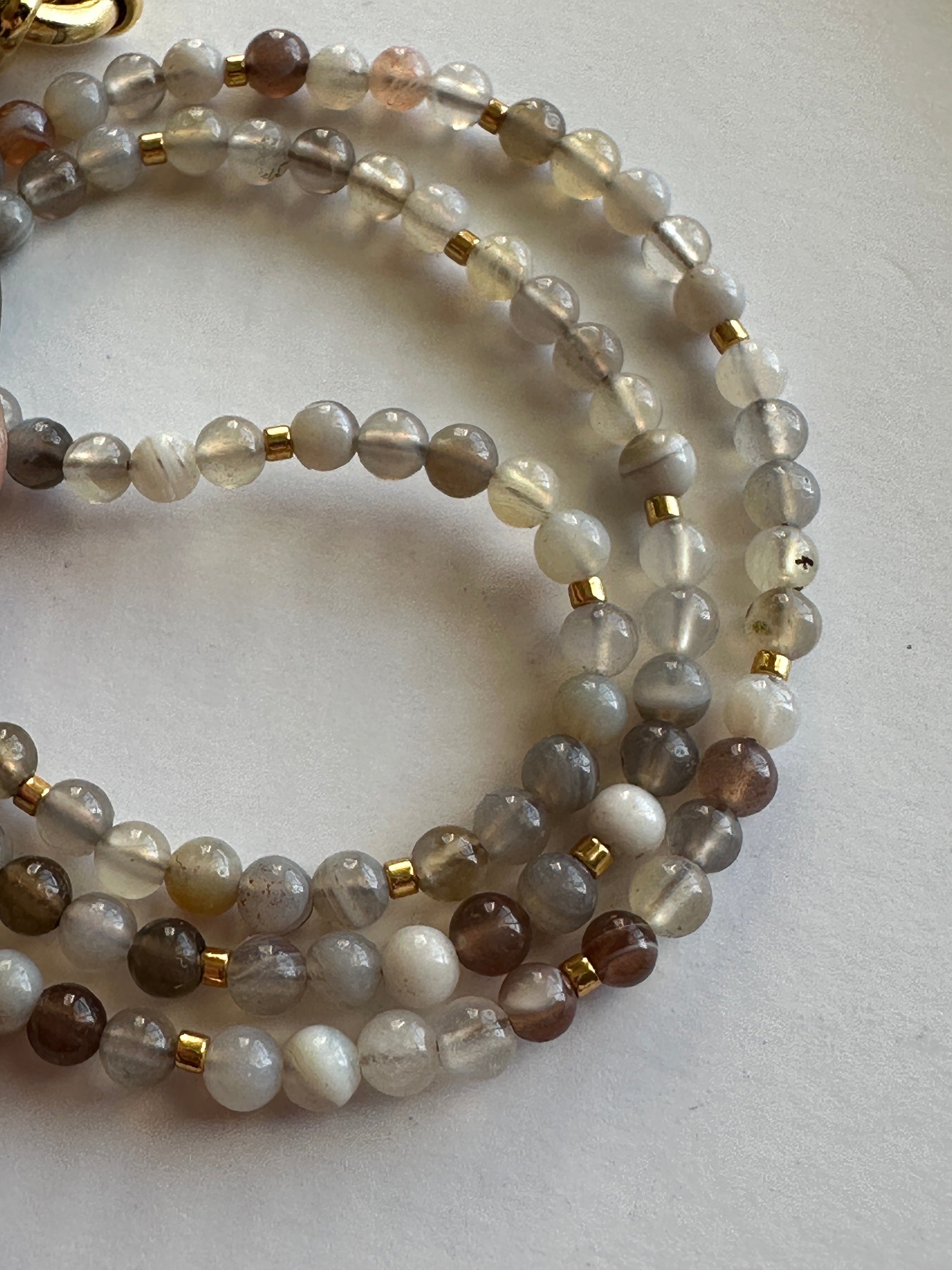 Close-up of the Marula necklace by Auréad Designs showing multiple strands coiled together, highlighting the natural gray, taupe, and warm neutral banding variation of Botswana agate beads with galvanized gold spacers