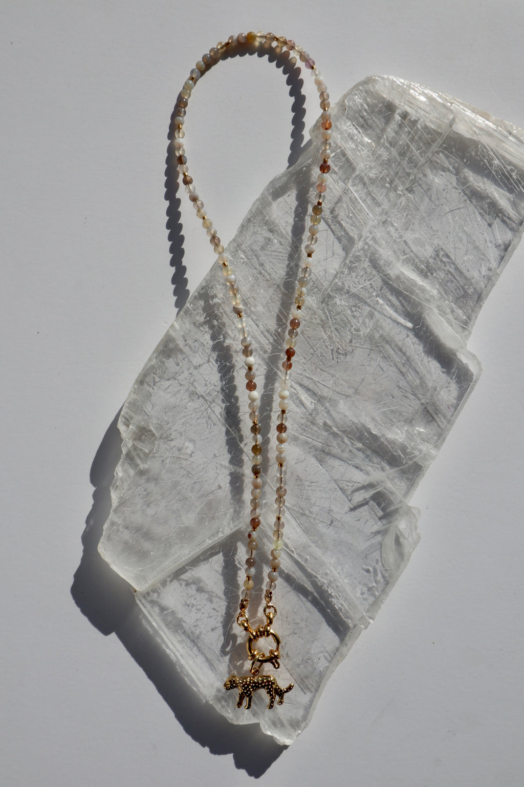 Marula necklace by Auréad Designs, featuring Botswana agate gemstone beads, galvanized gold spacer beads, and a gold stainless steel leopard charm with a sailor spring clasp, laid flat on a white selenite slab